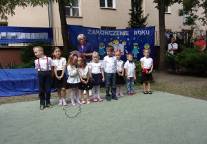 dzieci z różnych grup w galowych strojach na tle dekoracji z okazji Zakończenia Roku Przedszkolnego