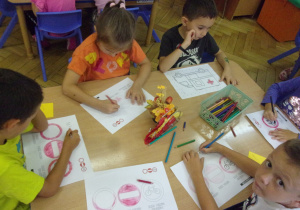 Grupa dzieci siedzi przy stoliku i koloruje znaki drogowe.