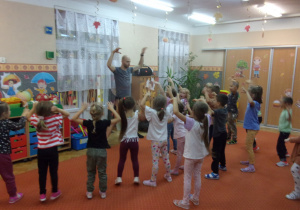 Instruktor i dzieci podnoszą wysoko ręce.
