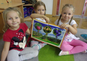 Trzy dziewczynki prezentują plansze z owocami.