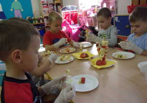 Dzieci siedzą przy stoliku i nakłuwają owoce na patyczki drewniane