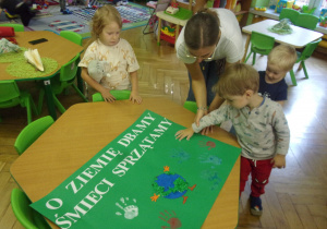 Chłopiec stoi obok papieru z odciśniętymi dłońmi.