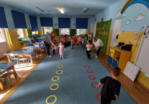 Dzieci uczestniczą w zabawie ruchowej na dywanie.