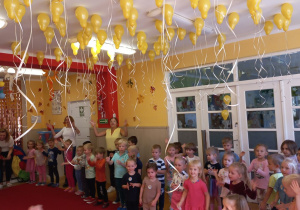 Dzieci tańczą a nad nimi są żółte balony.
