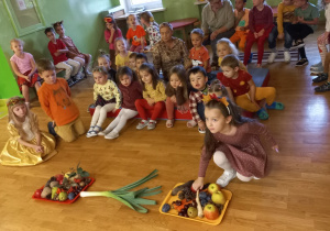 Dziewczynka w sukience z opaską z liśćmi podnosi pietruszkę.