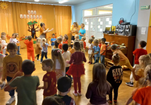 Przedszkolaki przebrani w kolory jesieni tańczą.