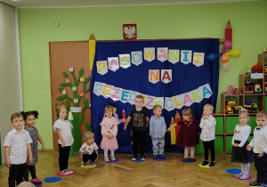 Grupa dzieci stoi wspólnie przed dekoracją.