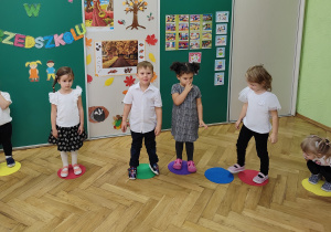 Grupa dzieci stoi na kolorowych, płaskich kołach.