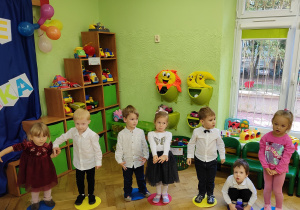 Grupa dzieci stoi obok siebie w kole.