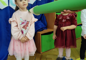Dziewczynka stoi na fioletowym kółku. Zielony ołowek dotyka ramienia dziewczynki.