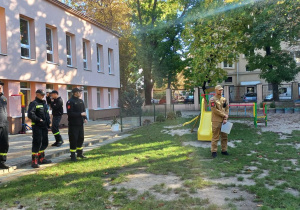 Strażacy stoją przed dziećmi.