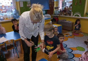 Pani Agnieszka maluje chłopczykowi rękę na zielono.