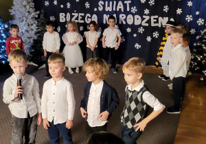 Chłopiec w koszuli i szarych spodniach mówi wiersz do mikrofonu.