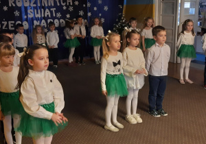 Dziewczynka w białej bluzce i zielonej spódniczce mówi swój wiersz.
