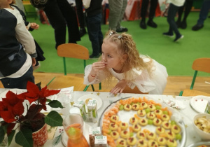 Dziewczynka w białej sukience je ciasteczko.