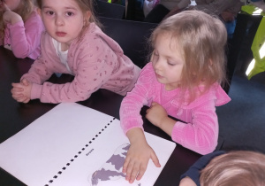 Dziewczynka dotyka kartki na której narysowana jest krowa.