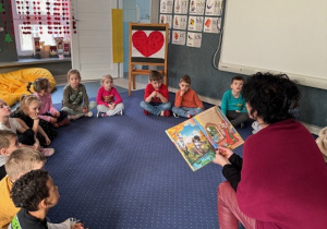 Juniorzy siedzą w kole na dywanie i słuchają opowiadania.