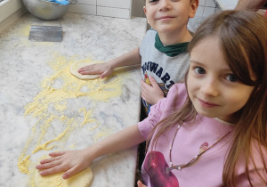 Dziewczynka i chłopiec przygotowują ciasto na pizzę.