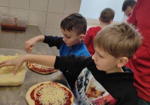 Chłopcy dodają ser na pizze.