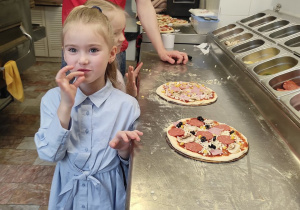 Dziewczynka stoi obok swojej gotowej pizzy.