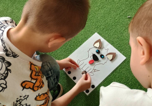 Chłopcy przyklejają części ciała pieska na kartce.