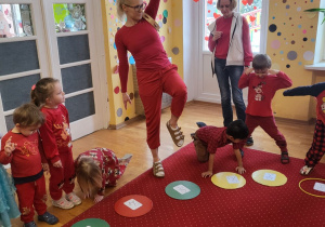 Dzieci ustawione w kole wykonują pozycję, którą przedstawia im ich karta na dywanie.