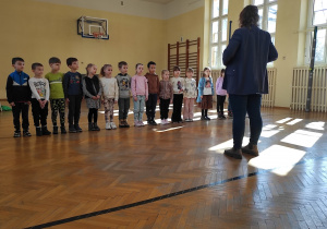 Juniorzy ustawieni w rzędzie słuchają Pana na sali gimnastycznej.