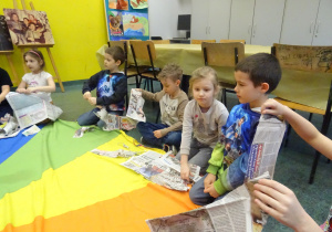 Inna grupa dzieci drze kawałki gazety na kolorową chustę.