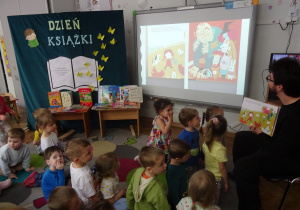 Dzieci siedzą na dywanie i oglądają prezentację o książkach.