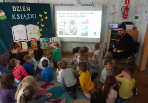 Dzieci siedzą na dywanie i oglądają prezentację.