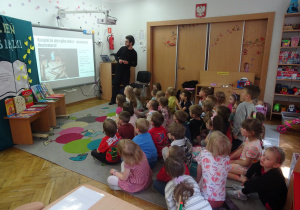 Dzieci siedzą na dywanie i oglądają prezentację o tworzeniu książek.