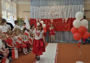 Dziewczynka z wiankiem na głowie idzie wzdłuż sali.