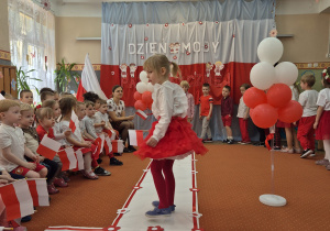 Inna dziewczynka trzyma flagę Polski i idzie wzdłuż sali.