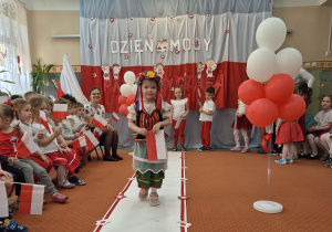 Dziewczyna w stroju ludowym idzie wzdłuż sali.