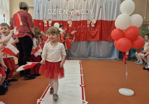 Inna dziewczynka trzyma flagę Polski i idzie wzdłuż sali.