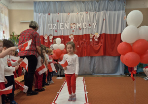 Dziewczynka trzyma flagę Polski i idzie wzdłuż sali.