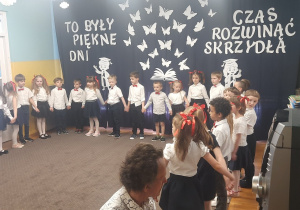 Dzieci stoją w półkolu i trzymają się za ręce.