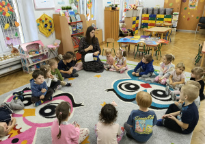 Dzieci siedzą w kole na dywanie.