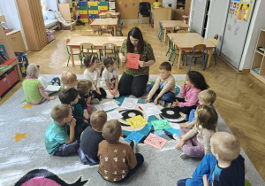 Nauczyciel siedzi na dywanie i trzyma w rękach czerwoną kartkę.