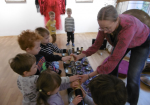 Osoba prowadząca warsztaty podaje instrument dziecku do ręki.