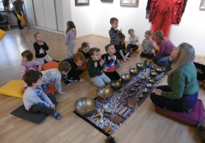 Dzieci siedzą przy instrumetach muzycznych.