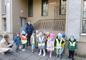Grupa dzieci i pani z obsługi stoją przy budynku poczty.