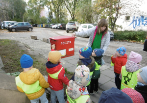 Dzieci i nauczycielka stoją przy czerwonej skrzynce pocztowej.
