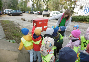 Dzieci dotykają czerwoną skrzynkę pocztową.