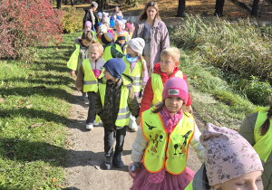 Grupa dzieci idzie pomiedzy trawami.