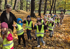 Grupa dzieci przyglada się liściom w parku.