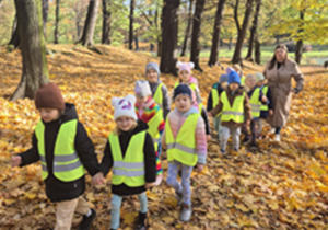 Dzieci razem z nauczycielem idą przez liście.