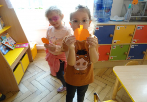 Dwie dziewczynki stoją trzymając w ręku papierową dynię.