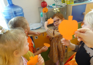 Dzieci stoja obok siebie i trzymają papierowe dynie.