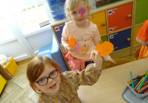 Dwie dziewczynki trzymają papierowe dynie.